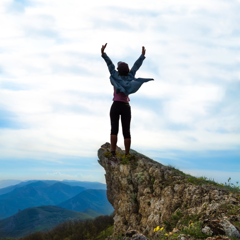 A woman excitedly raising her arms on a mountain.